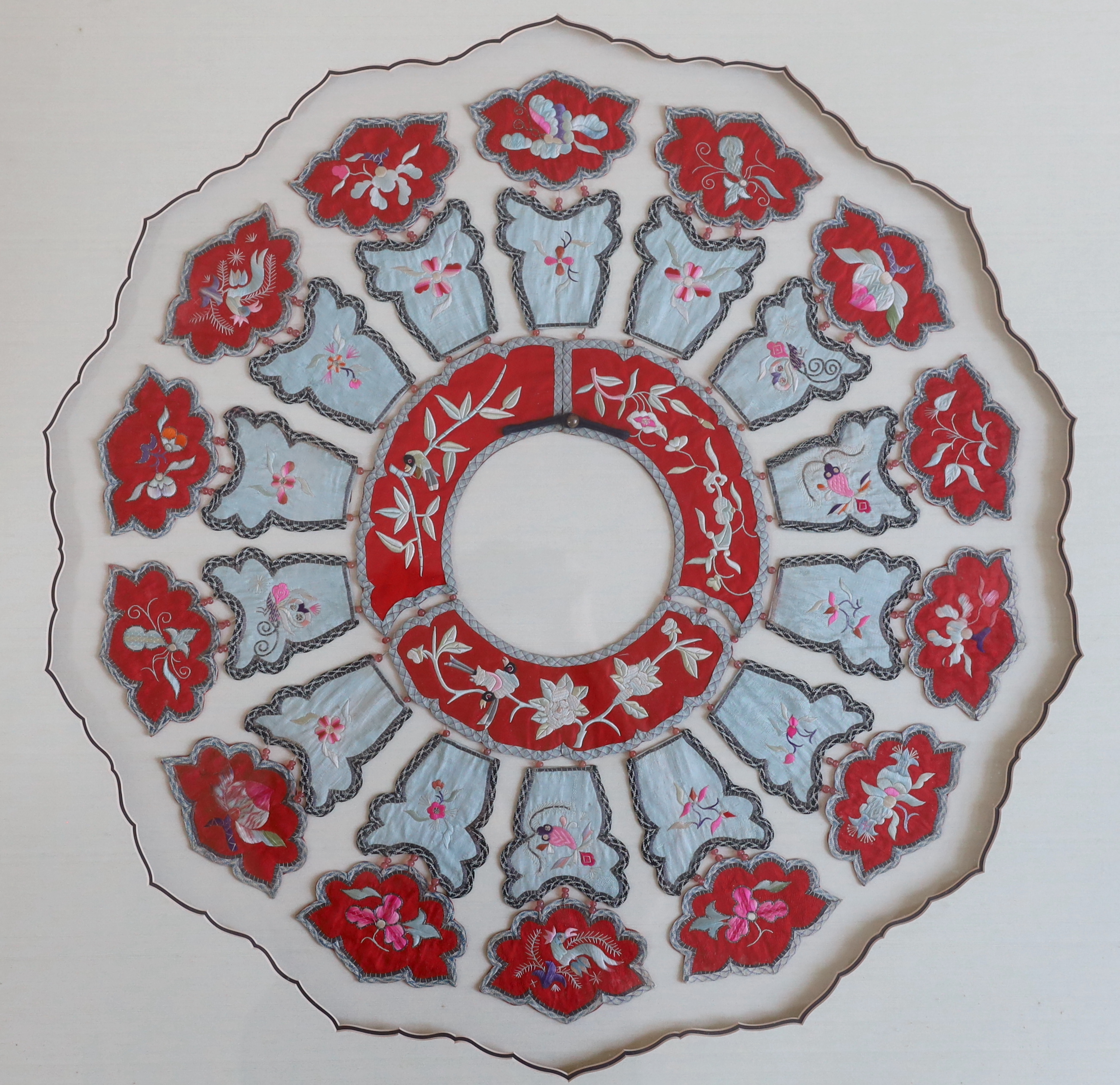 A large early 20th century Chinese silk embroidered collar, made with fourteen decorative and embroidered hanging panels attached to a circular central collar with bead attachments, set within an ornate mount and framed,